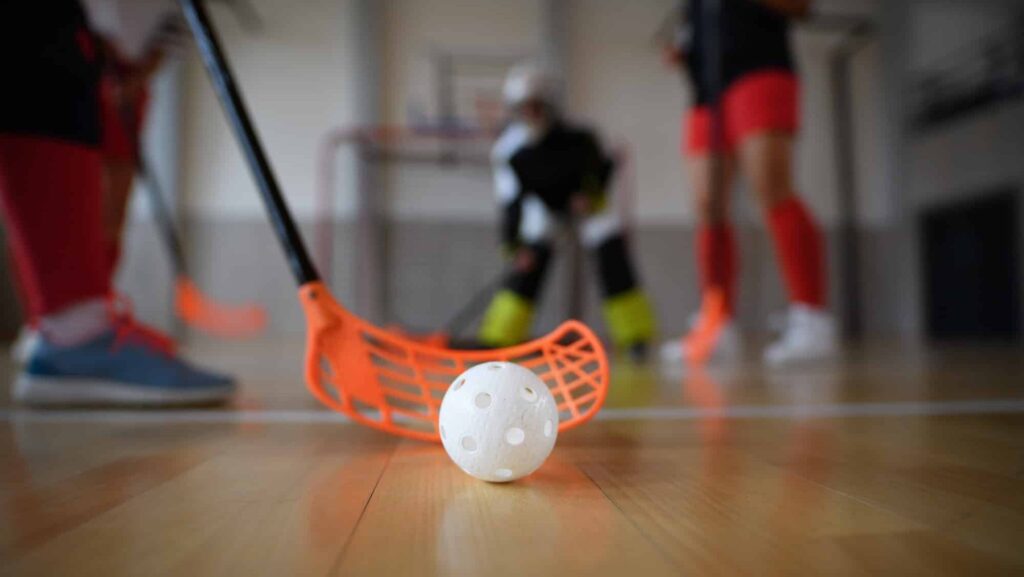Close-up of floorball stick and ball during woman floorball match in gym.